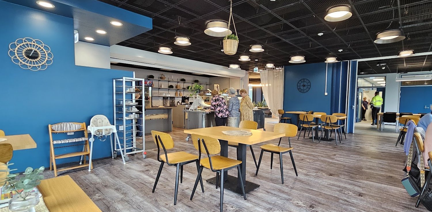 Cafe Hillan sali: sininen seinä, puiset pöydät ja keltaiset tuolit, järvinäkymä ikkunoista
